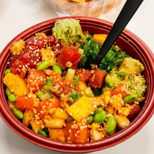 Close-up of a colorful poke bowl with tuna, mango, edamame, and avocado in a red bowl.