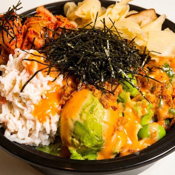 A colorful poke bowl with kimchi, crab salad, avocado, edamame, and seaweed on rice.